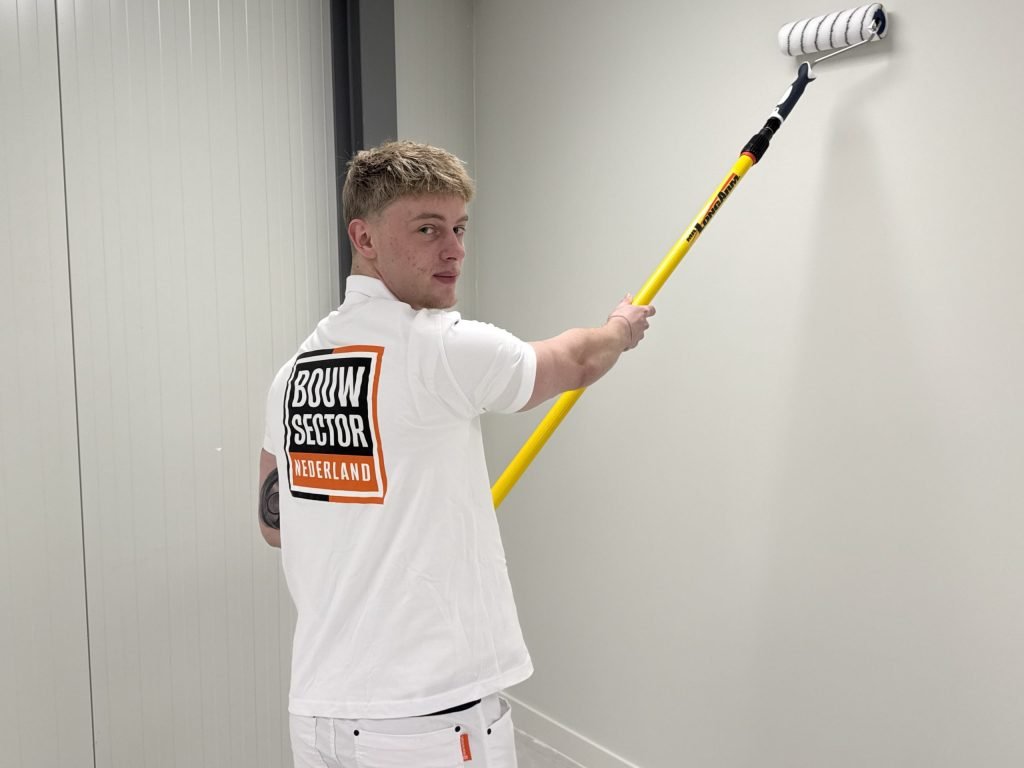 Schilder van Bouwsector Nederland kijkt over zijn schouder terwijl hij een witte wand in een gang rolt