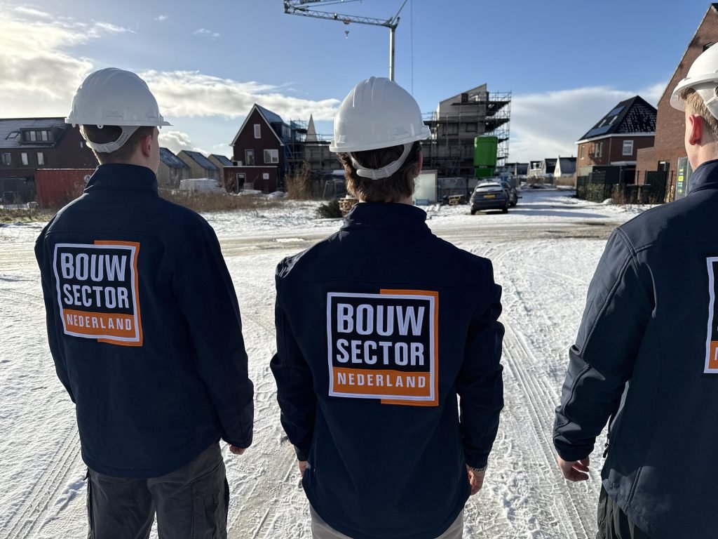 Drie mannen in werkkleding met het logo van Bouwsector Nederland op de rug voor een rij huizen