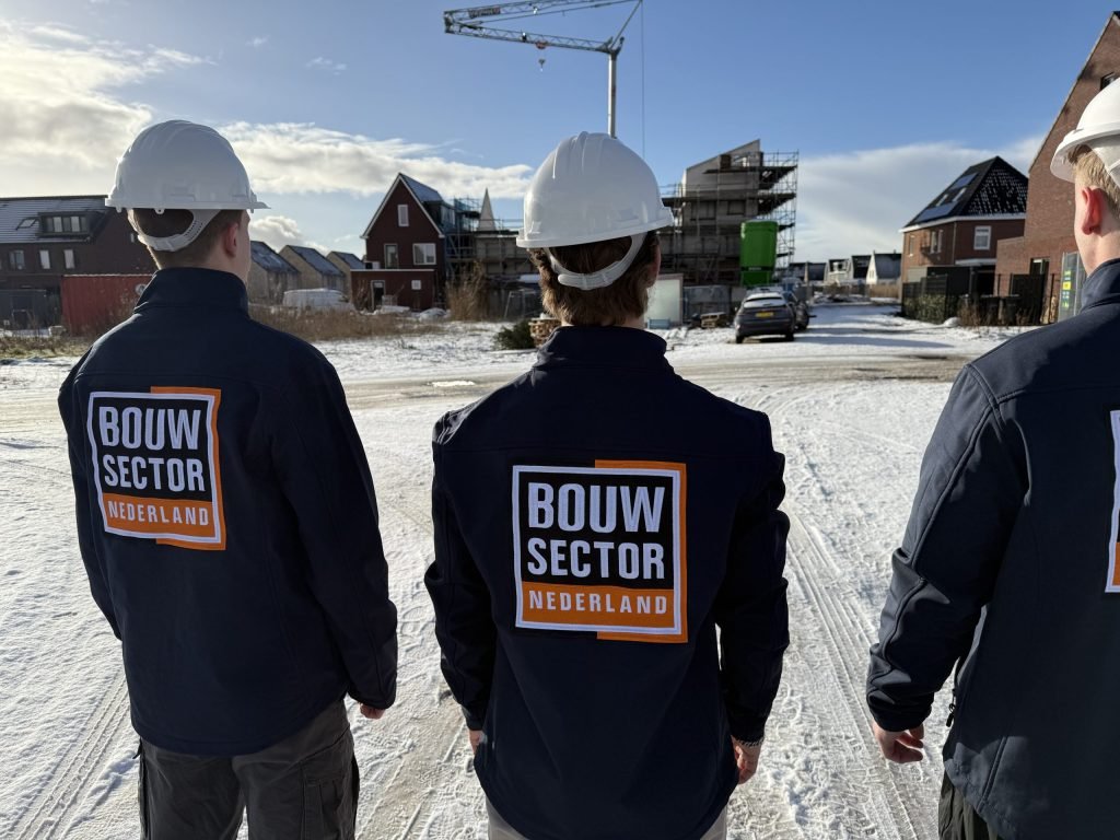 Vakmensen van Bouwsector Nederland met witte helm staan bij een nieuwbouwwijk met kraan en steigers